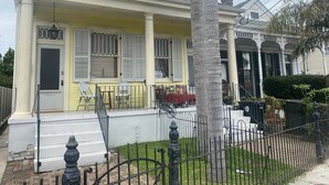 A two-story house with a yellow facade, a front porch with a railing, and a palm tree in the foreground. - West Riverside Shotgun Near Audubon Park (New Orleans)