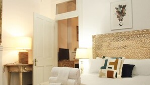 A hotel room with a neatly made bed, a bedside table with a lamp, a television, and a decorative headboard. - West Riverside Shotgun Near Audubon Park (New Orleans)
