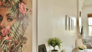 A living room with a large floral painting, a coffee table with a vase of flowers, and a sofa. - West Riverside Shotgun Near Audubon Park (New Orleans)