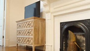 A wooden dresser with drawers, a television on top, and a fireplace with a metal poker. - West Riverside Shotgun Near Audubon Park (New Orleans)