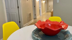 Un comedor con una mesa blanca, un cuenco rojo y sillas amarillas.