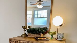 Un tocador de madera con un diseño hexagonal decorativo, un espejo redondo, un ventilador de techo y una pequeña planta en maceta.
