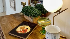 Una mesa de madera con un libro, una lámpara, un cuenco decorativo y una planta pequeña.