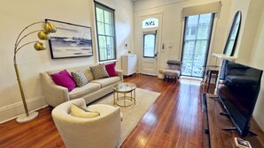 A living room with a sofa, armchair, coffee table, TV, and a painting on the wall.