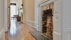 A hallway with a brick fireplace, wooden flooring, and a door leading to another room.