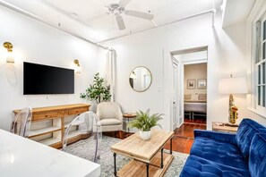 A modern living room with a flat-screen TV, a wooden coffee table, a blue sofa, and a dining area with a table and chairs.