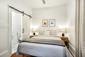 A bedroom with a bed, bedside tables, a door, and two framed pictures on the wall.