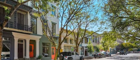 A street lined with multi-story residential buildings, parked cars, and trees.