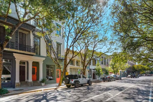A street lined with multi-story residential buildings, parked cars, and trees.