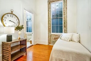 A bedroom with a bed, a wooden nightstand with a lamp, a large wall clock, and a window with a view.