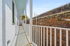 A narrow corridor with a white railing, a brick wall, and a clear sky.