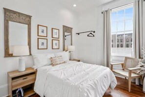 A bedroom with a large bed, bedside tables, a chair, and a window with a view.
