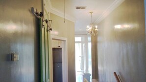Ein Flur mit einer zur Küche führenden Tür, einer Chandelierleuchtre und Blick in einen weiteren Raum.