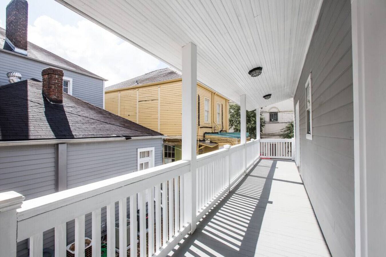 Een overdekt terras met een witte balustrade, uitzicht op omliggende huizen en een heldere lucht.