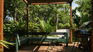 A wooden deck with a bench, a grill, and lush greenery.
