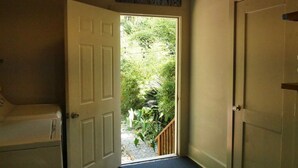 A room with a white door leading to a garden, a wooden bench, and a sign above the door reading 'FRENCH QUARTER'.