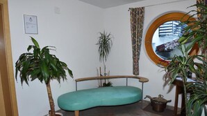 A room with a curved teal sofa, a potted plant, a small table, and a window with a view of a building. - Retreat in Samnaun Alps (Samnaun)