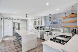 A modern kitchen with white cabinetry, a central island, stainless steel appliances, and a backsplash with a mosaic tile pattern.