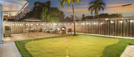 A backyard with a putting green, outdoor seating, and a wooden fence.