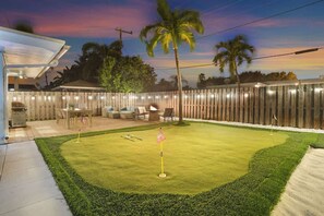 Un jardin avec un terrain d’entraînement au golf, un espace salon extérieur et une clôture en bois.