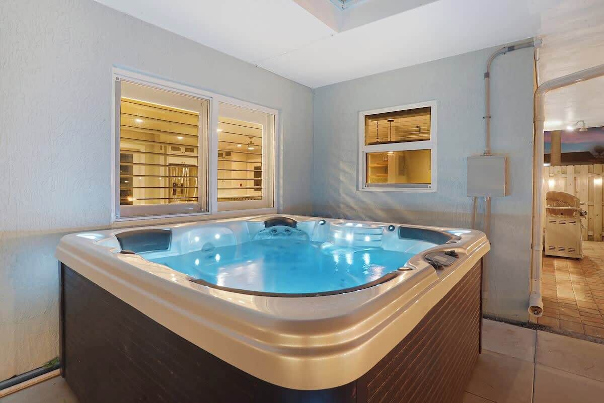 A hot tub in a room with a window, a wall-mounted shelf, and a visible electrical outlet.