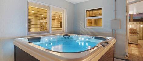 A hot tub in a room with a window, a wall-mounted shelf, and a visible electrical outlet.
