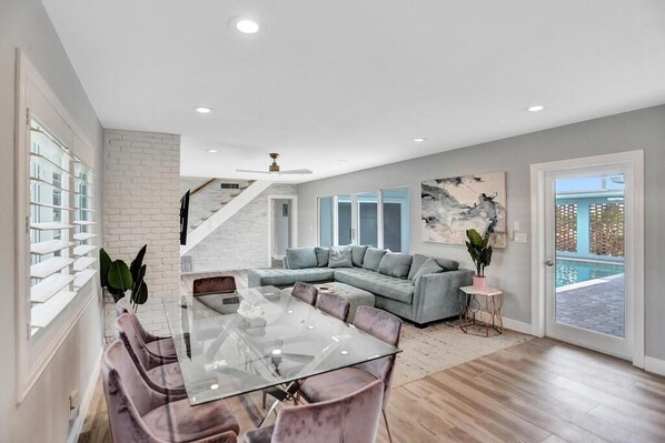 A spacious living area with a glass dining table, a gray sectional sofa, and a view of a pool.