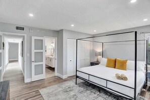 A modern bedroom with a four-poster bed, a walk-in closet, and a bathroom with a shower.