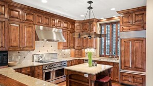 A kitchen with wooden cabinets, a granite countertop, stainless steel appliances, and a hanging light fixture.