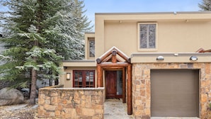 A modern house with a stone entrance, a garage, and a large evergreen tree in the background.