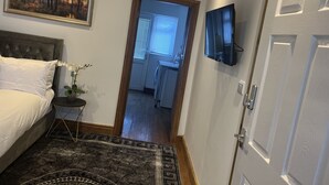 Un dormitorio con cama, mesita de noche, planta en maceta, cuadro y televisor en la pared.