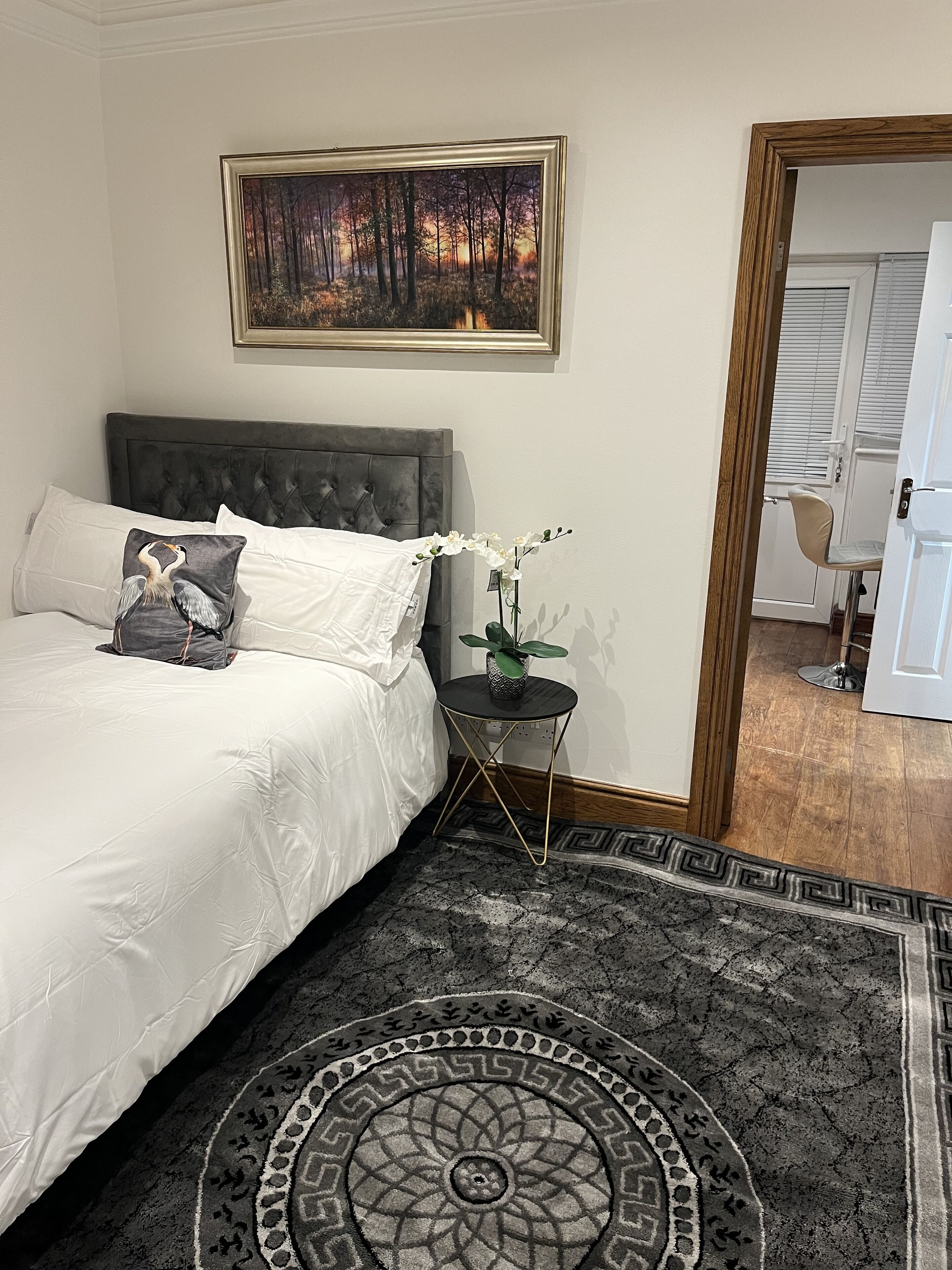 A bedroom with a bed, a nightstand, a framed painting, and a view of a hallway.