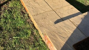 Un sendero de piedra que conduce a una entrada de ladrillo, rodeado de césped y arbustos bien cuidados.