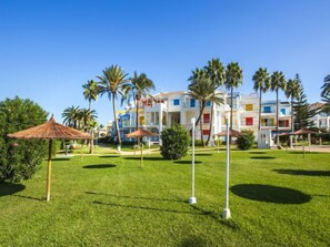 Ein Hotel mit gepflegter Rasenfläche, Palmen und farbenfrohen Gebäuden im Hintergrund.