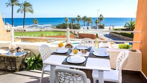 A balcony with a table set for two, overlooking a beach with palm trees and a clear blue sky. - Deltamar by Interhome (Jávea)