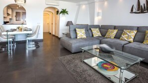 A modern living room with a grey sofa, a glass coffee table, and a dining area with a white table and chairs. - Deltamar by Interhome (Jávea)