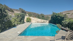 A rectangular pool with clear blue water, surrounded by stone walls and greenery, with a stone deck and lounge chairs. - Parian Beach House with Pool Access, walk to the Beach (Paros)