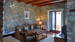 A cozy living room with a stone wall, wooden ceiling beams, a sofa, a coffee table, and a television. - Parian Beach House with Pool Access, walk to the Beach (Paros)