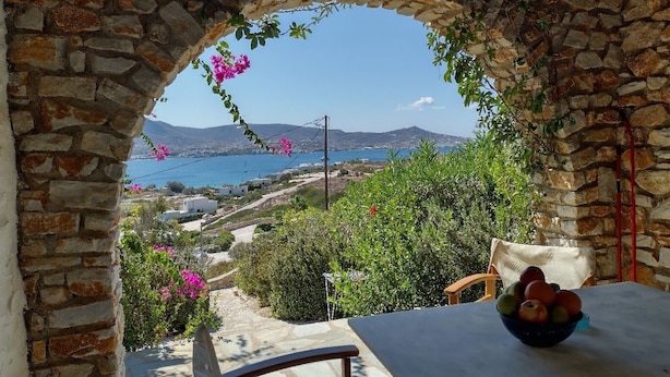 A stone archway overlooking a coastal landscape with a table and chairs, a bowl of fruit, and blooming flowers. - Parian Beach House with Pool Access, walk to the Beach (Paros)