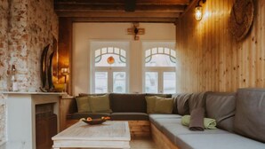 Un salon chaleureux avec un plancher en bois, une table basse blanche, un canapé gris agrémenté de coussins verts et une cheminée ornée d’un miroir et d’objets décoratifs.