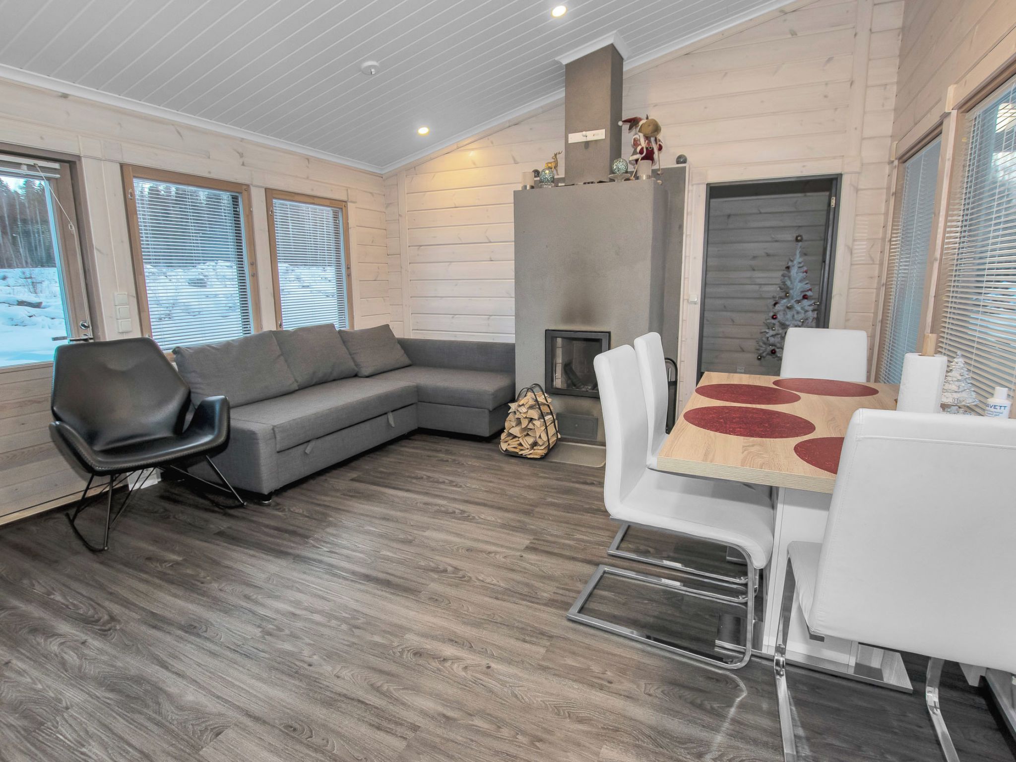 A modern interior with a grey sofa, a dining table with red accents, and a fireplace.