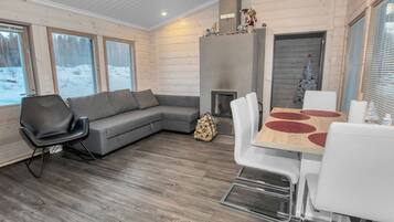 A modern interior with a grey sofa, a dining table with red accents, and a fireplace.