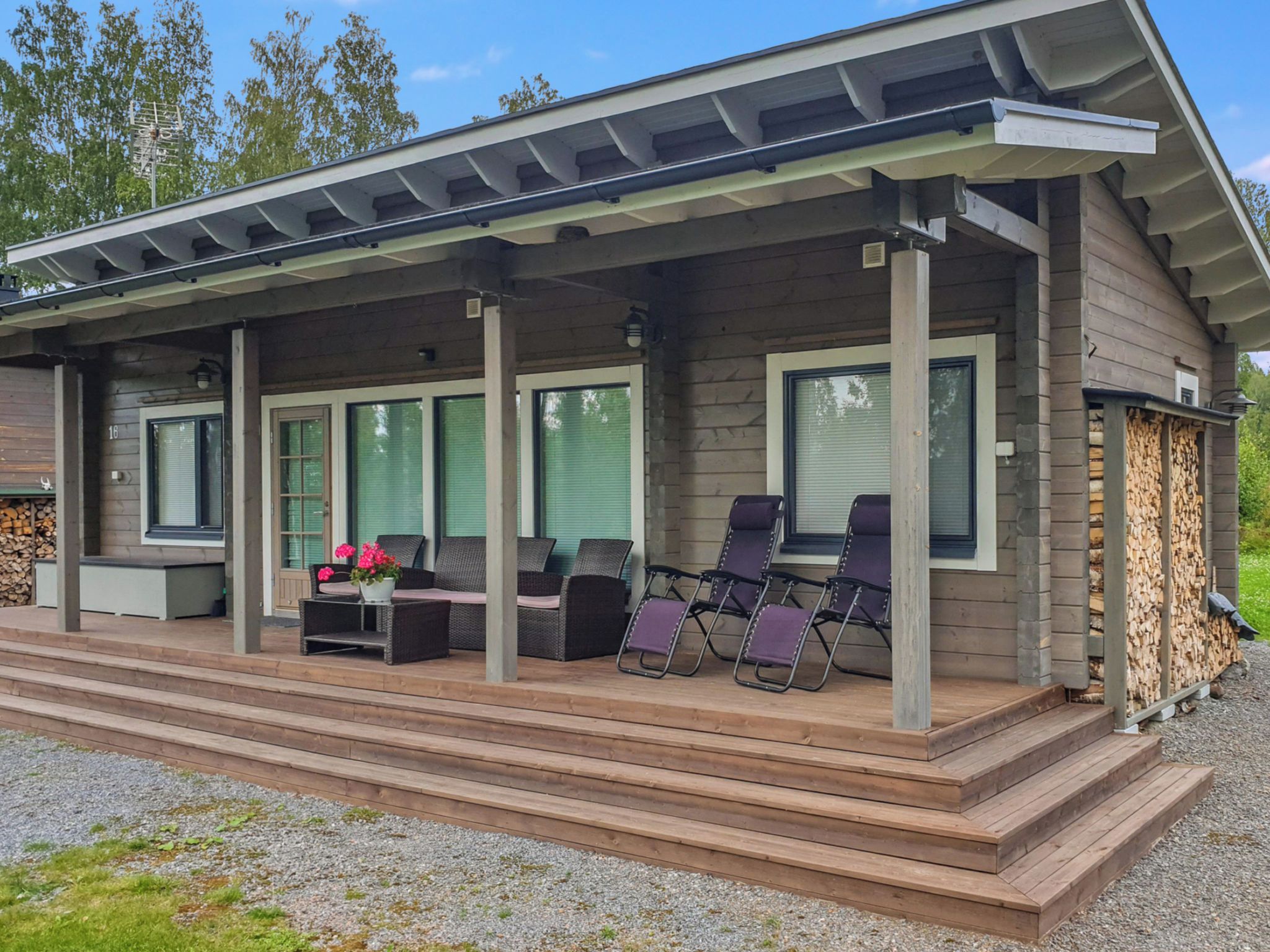 A wooden cabin with a covered porch, outdoor seating, and a stack of firewood.
