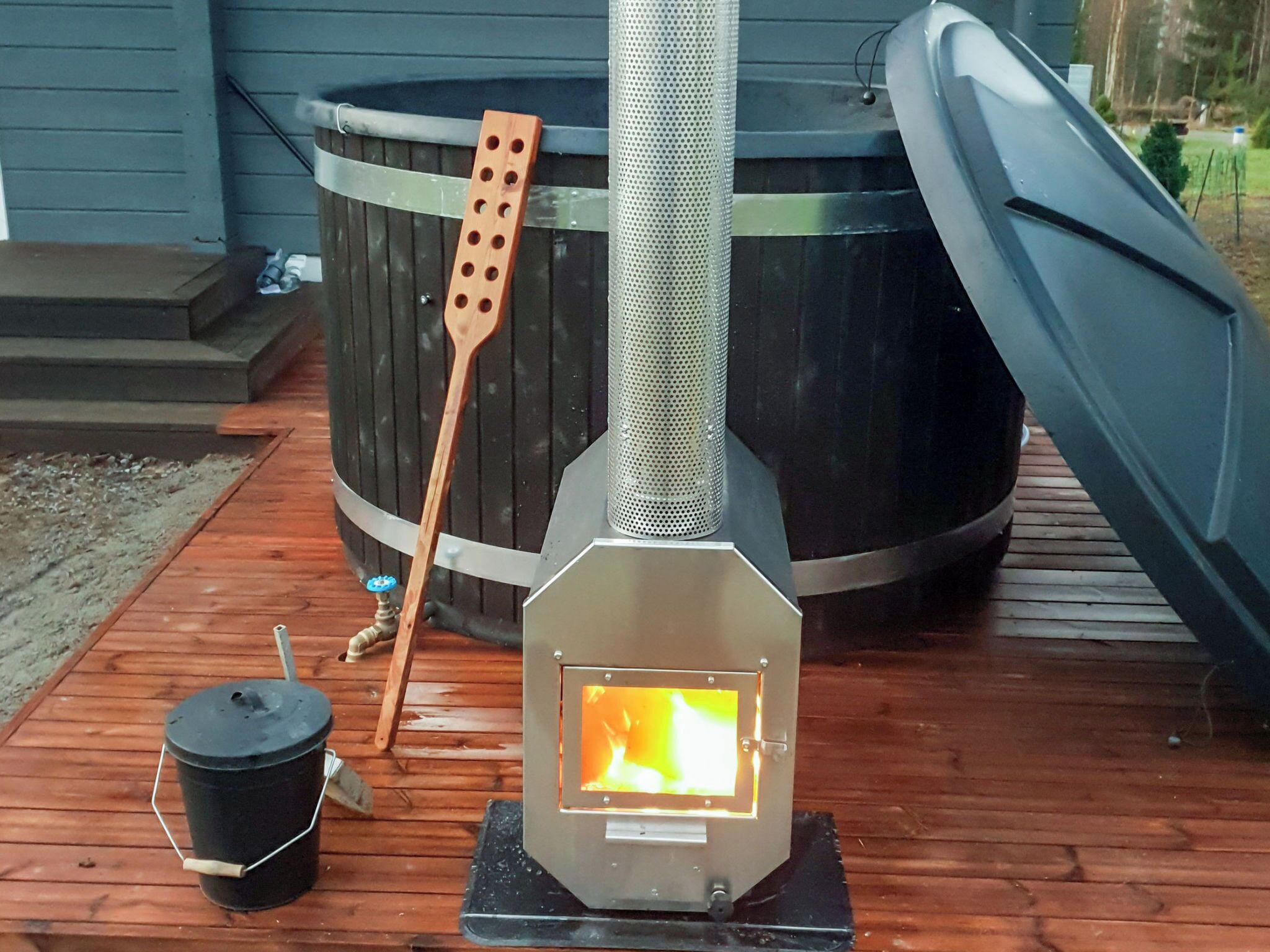 Puuhellassa näkyy avotuli, siinä on metallinen savupiippu ja puinen kauha.