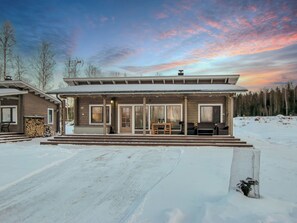 A modern house with a covered porch, a fireplace, and a view of a snowy forest.