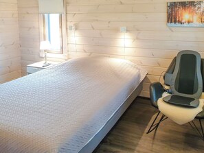 A single bed with a textured mattress, a bedside table with a lamp, a chair with a cushion, and a painting on the wall. - Adeli holiday cottage ellivuori by Interhome (Sastamala)