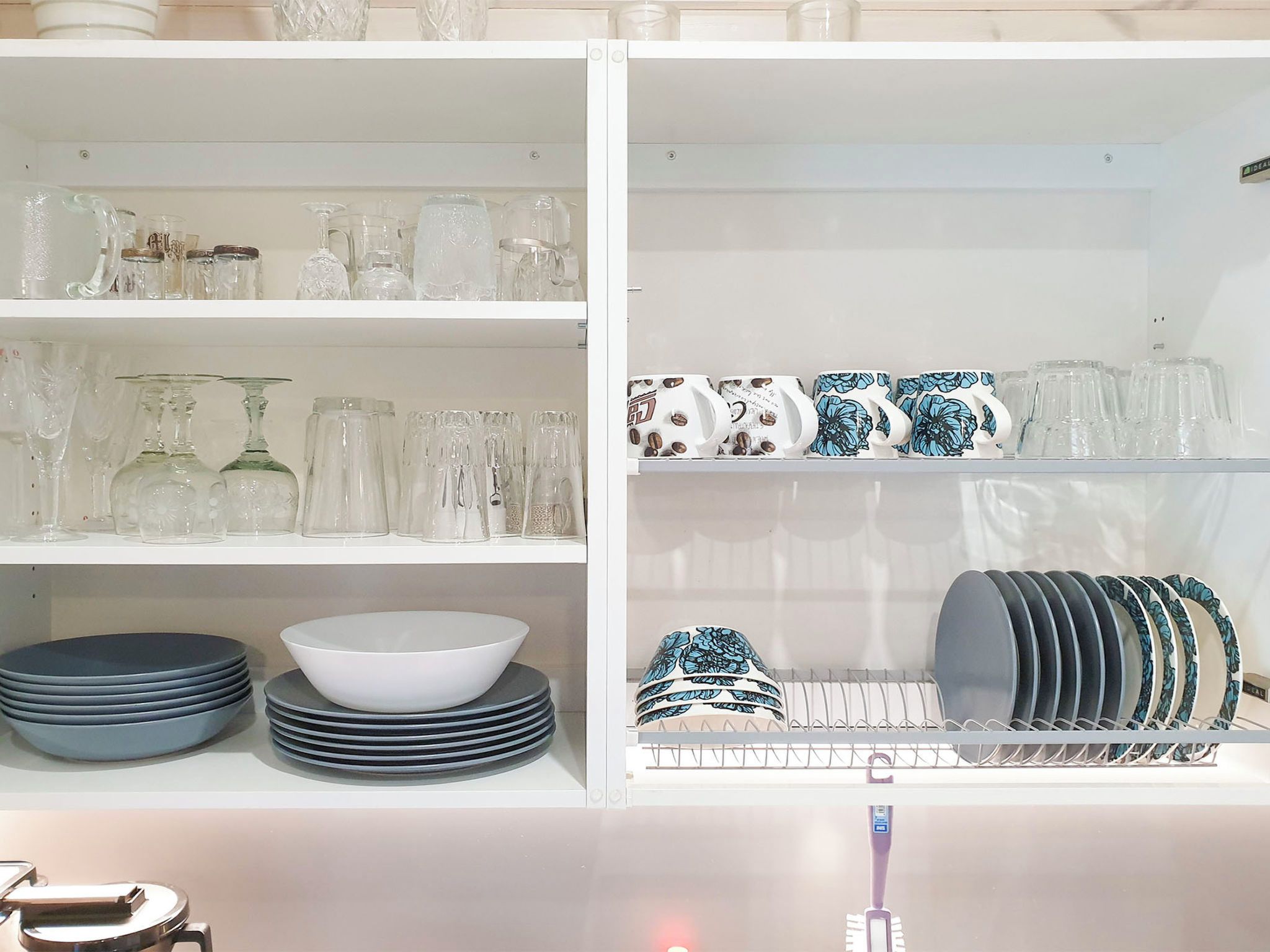 Een keuken met witte kastjes, drinkglazen, borden en kommen.