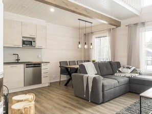 Cocina moderna con microondas, lavavajillas y armarios de madera. Hay un comedor con mesa y sillas, y un sofá gris en la sala.
