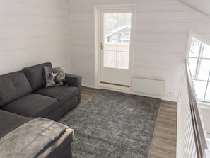 Una sala de estar moderna con un sofá gris, un plaid estampado y vistas a través de una puerta blanca.