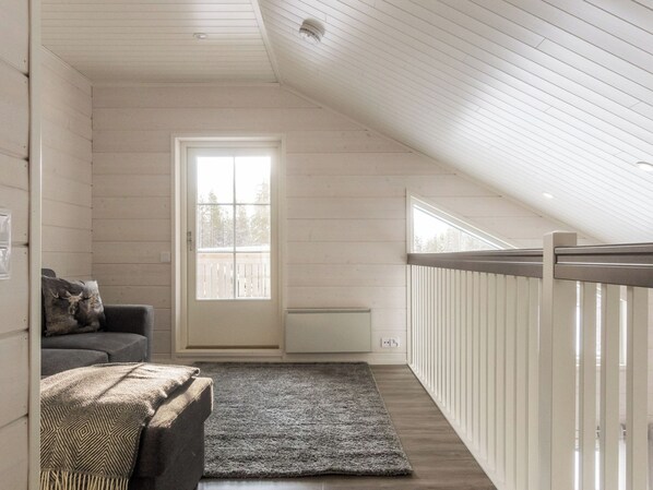 Una habitación con techo inclinado, una ventana con persianas, un radiador, un sofá gris y una alfombra estampada.